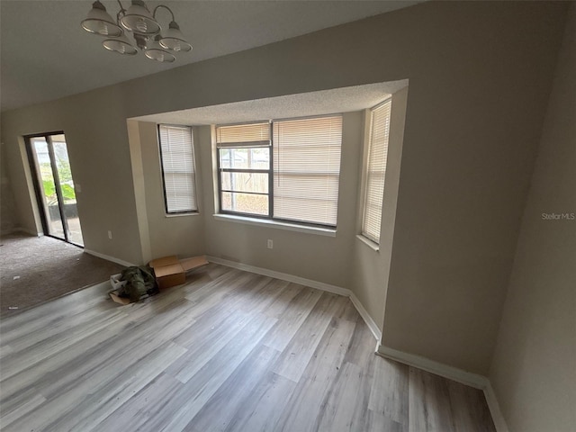 empty room featuring wood finished floors, baseboards, and a chandelier