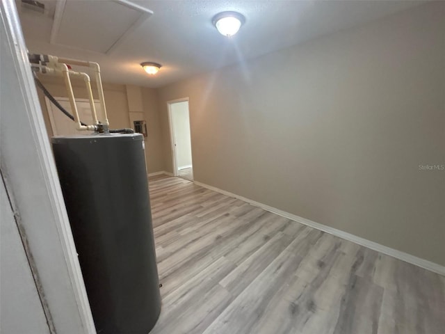 corridor featuring visible vents, gas water heater, light wood finished floors, baseboards, and attic access