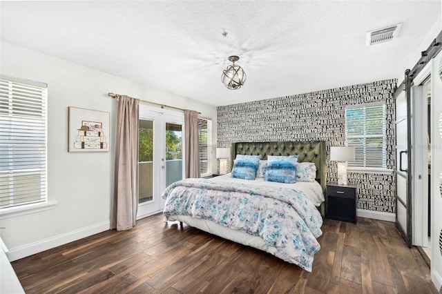 bedroom featuring a barn door, dark wood-style floors, access to exterior, and visible vents