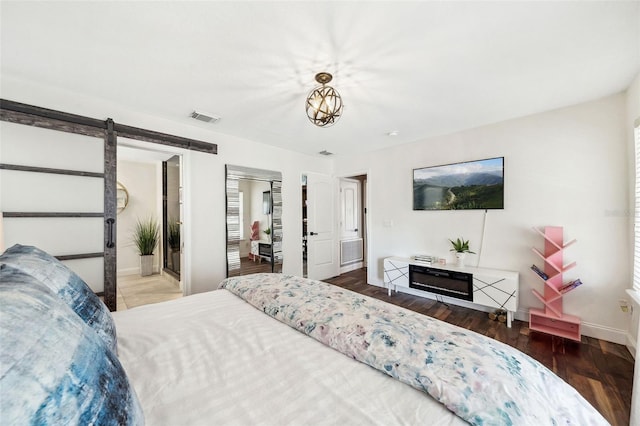 bedroom with a barn door, wood finished floors, visible vents, and baseboards