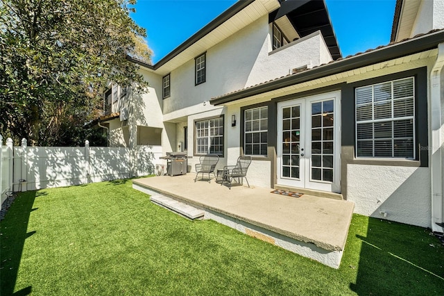 back of property featuring stucco siding, french doors, a lawn, and fence