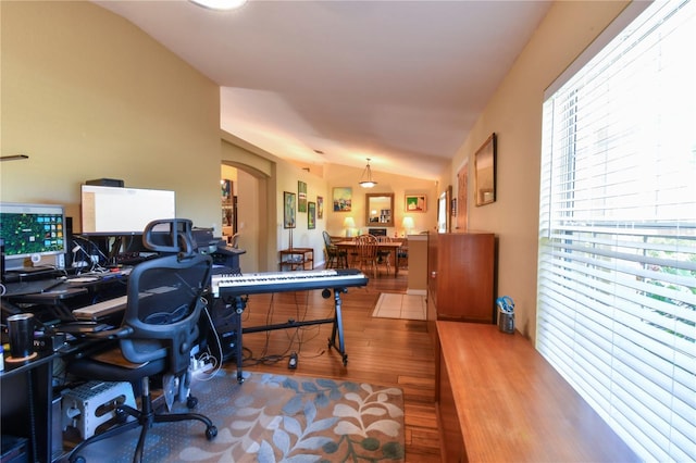 office space with arched walkways, lofted ceiling, and wood finished floors