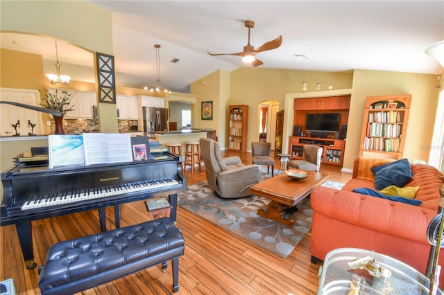 living area with arched walkways, light wood-style flooring, vaulted ceiling, and ceiling fan with notable chandelier