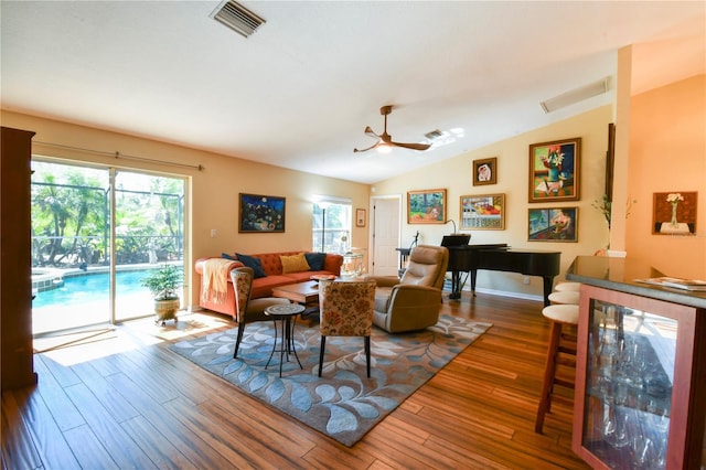 living area featuring a wealth of natural light, visible vents, lofted ceiling, and wood finished floors