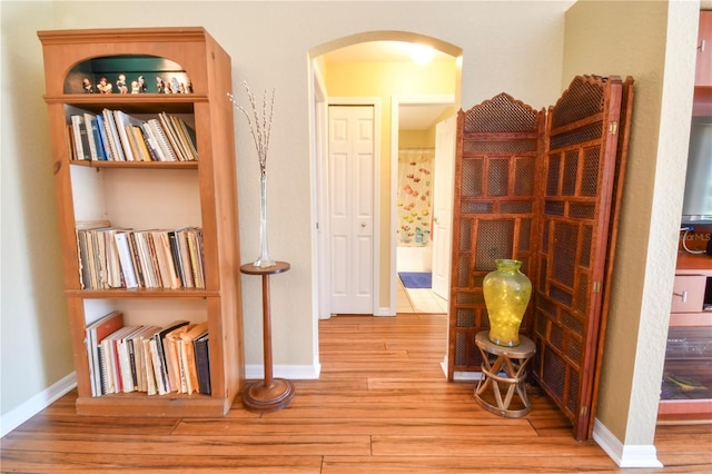 hallway with arched walkways, baseboards, and wood finished floors