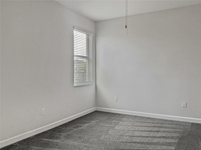 spare room with baseboards and dark carpet