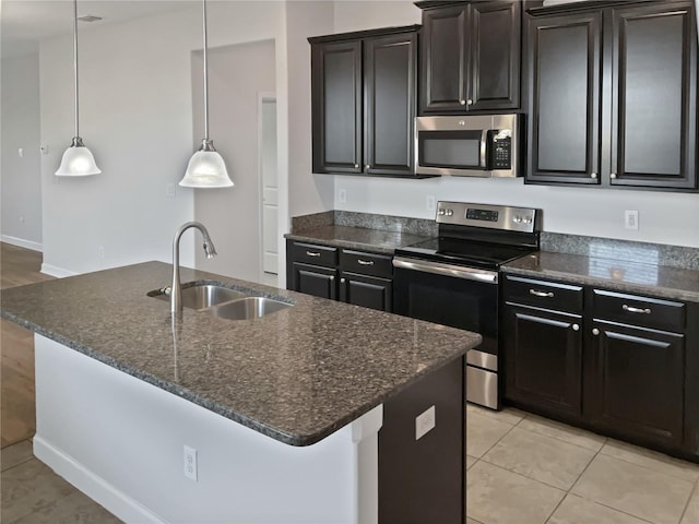 kitchen with dark stone countertops, light tile patterned floors, a kitchen island with sink, a sink, and stainless steel appliances