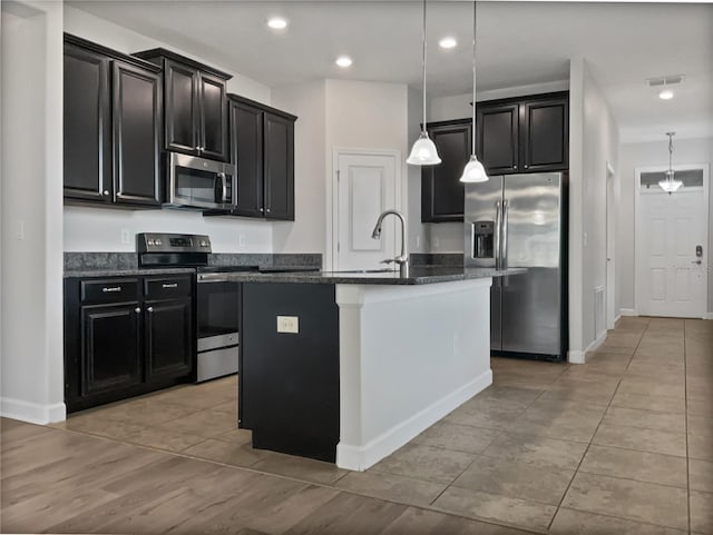 kitchen featuring stainless steel appliances, dark cabinetry, visible vents, and a center island with sink