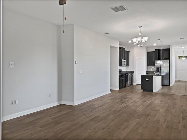 kitchen with a notable chandelier, dark countertops, open floor plan, dark wood-style floors, and appliances with stainless steel finishes