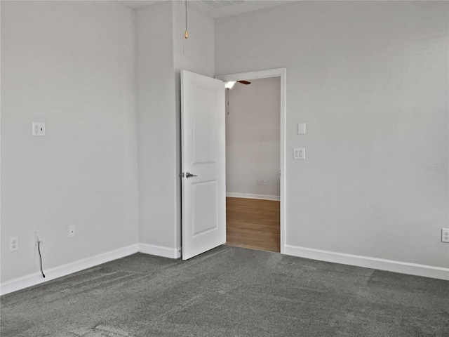 unfurnished room with ceiling fan, baseboards, and dark colored carpet