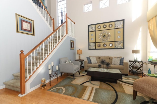 living room featuring stairway, a towering ceiling, baseboards, and wood finished floors