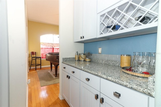 kitchen with light stone counters, baseboards, white cabinetry, and light wood finished floors