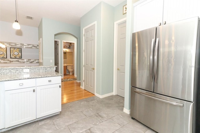 kitchen with decorative light fixtures, white cabinetry, freestanding refrigerator, arched walkways, and light stone countertops