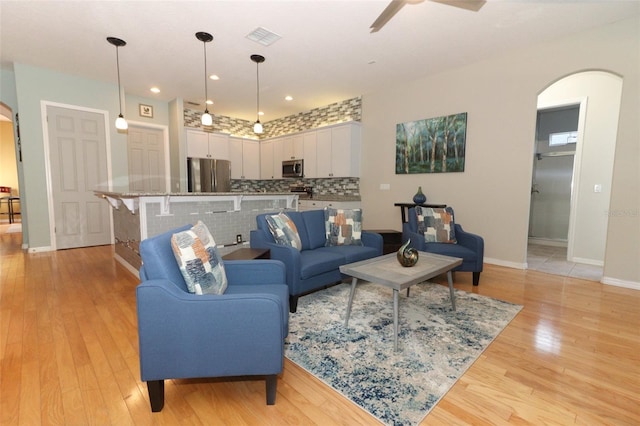 living area with visible vents, arched walkways, light wood-style floors, baseboards, and ceiling fan