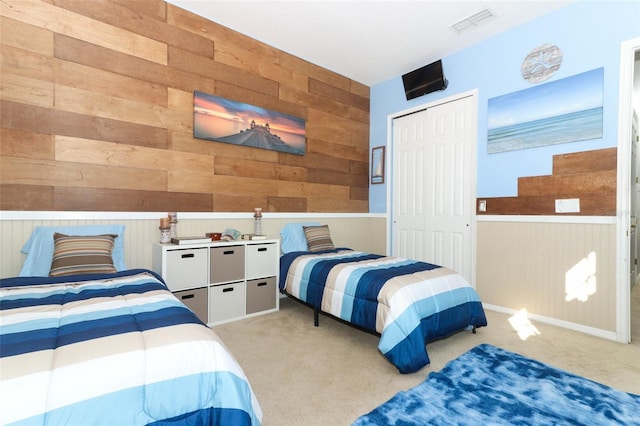 bedroom featuring visible vents, a closet, wood walls, and carpet flooring