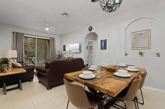 dining space with light tile patterned floors, baseboards, arched walkways, and ceiling fan with notable chandelier