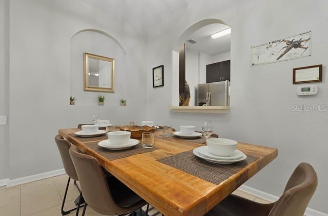 dining area featuring arched walkways, light tile patterned floors, visible vents, and baseboards