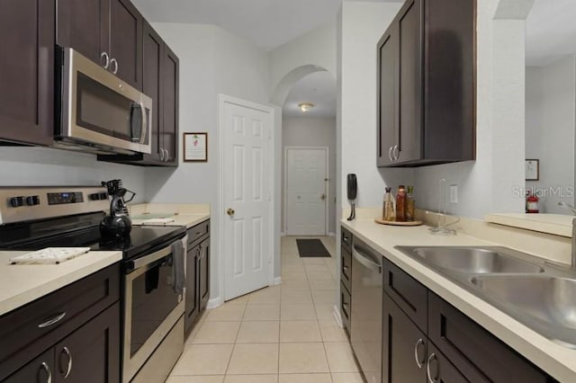 kitchen featuring light tile patterned floors, arched walkways, light countertops, dark brown cabinetry, and appliances with stainless steel finishes