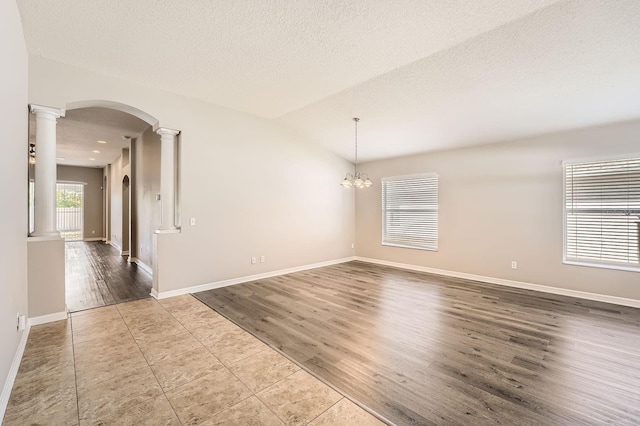 empty room featuring wood finished floors, baseboards, ornate columns, and a textured ceiling