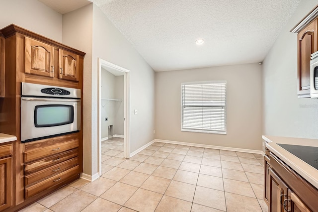 kitchen with oven, a textured ceiling, light tile patterned flooring, light countertops, and baseboards