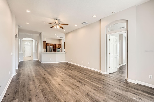 unfurnished living room with dark wood finished floors, visible vents, a ceiling fan, and arched walkways