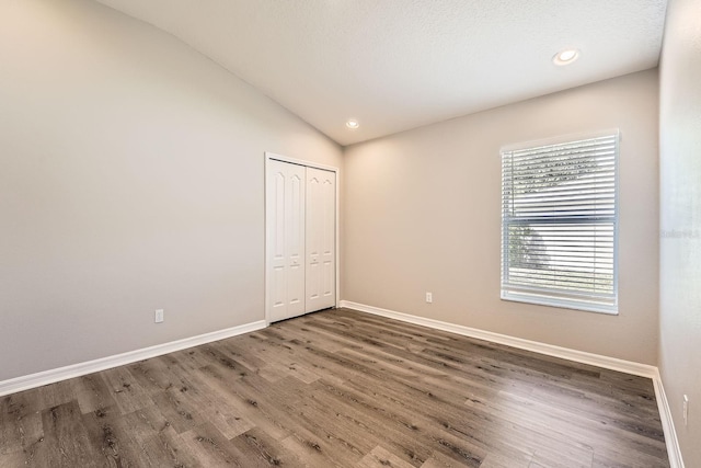 unfurnished bedroom with vaulted ceiling, wood finished floors, baseboards, and a closet