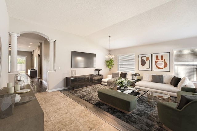 living area with baseboards, vaulted ceiling, arched walkways, a textured ceiling, and ornate columns