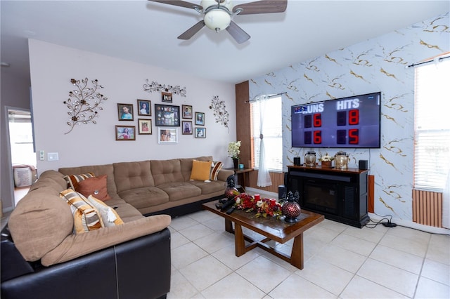 living area with wallpapered walls, a glass covered fireplace, light tile patterned floors, and ceiling fan