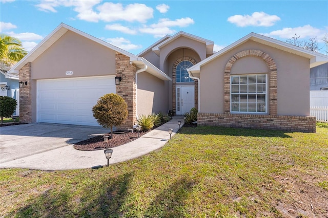 view of front of home featuring stucco siding, driveway, a front yard, a garage, and brick siding