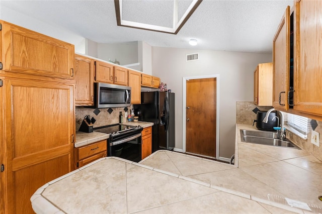 kitchen featuring visible vents, black appliances, a sink, tile patterned flooring, and vaulted ceiling