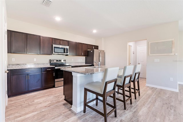 kitchen with a kitchen bar, visible vents, light wood-style flooring, dark brown cabinets, and appliances with stainless steel finishes