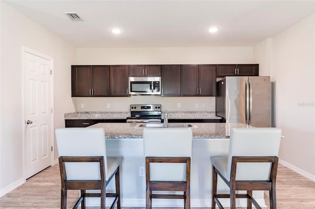 kitchen featuring dark brown cabinetry, a sink, light wood finished floors, a kitchen breakfast bar, and stainless steel appliances