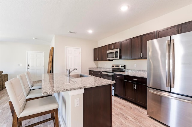 kitchen featuring visible vents, stainless steel appliances, a sink, light wood-style floors, and a breakfast bar area