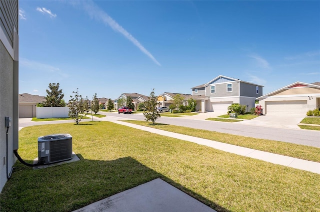 view of yard with fence, a garage, a residential view, driveway, and cooling unit