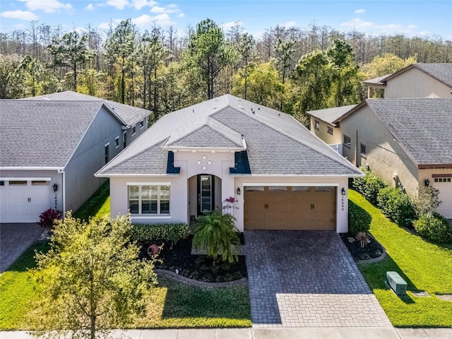 view of front of property featuring a front lawn, roof with shingles, stucco siding, decorative driveway, and an attached garage