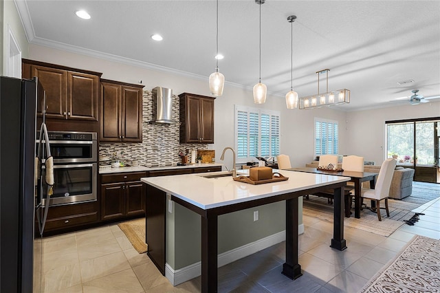 kitchen featuring black appliances, a sink, wall chimney range hood, light countertops, and decorative backsplash