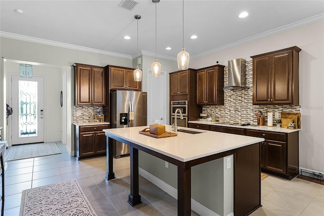 kitchen featuring an island with sink, a sink, light countertops, appliances with stainless steel finishes, and wall chimney exhaust hood