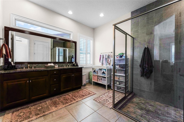 bathroom with a sink, a textured ceiling, a shower stall, tile patterned flooring, and double vanity