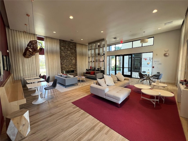 living room featuring a stone fireplace, recessed lighting, visible vents, and wood finished floors