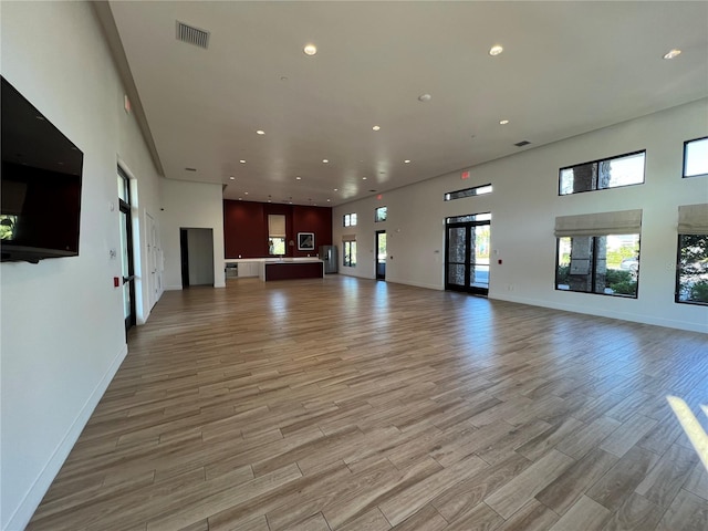 unfurnished living room featuring a high ceiling, recessed lighting, visible vents, and light wood finished floors