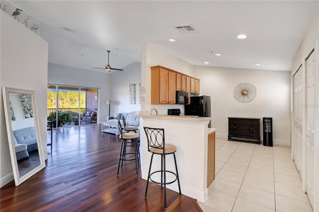 kitchen featuring visible vents, black appliances, open floor plan, a breakfast bar area, and lofted ceiling