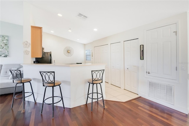 kitchen with a peninsula, a breakfast bar area, wood finished floors, and visible vents