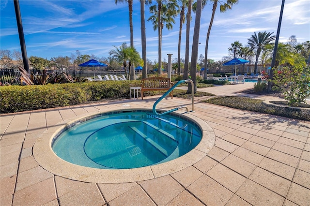 community pool with a patio, fence, and a hot tub