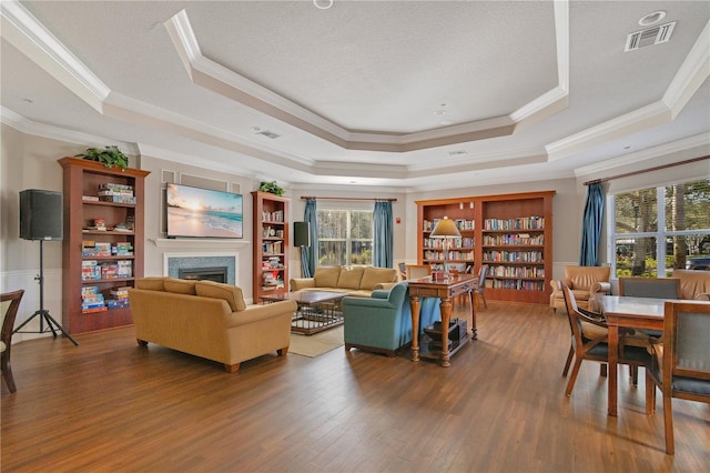 living room with visible vents, crown molding, a tray ceiling, a fireplace, and wood finished floors