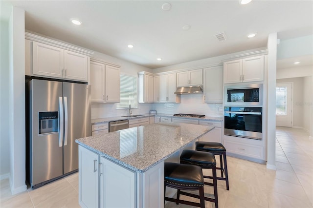 kitchen featuring visible vents, a kitchen island, under cabinet range hood, appliances with stainless steel finishes, and a sink