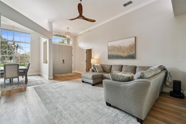 living area featuring visible vents, baseboards, ornamental molding, a towering ceiling, and wood finished floors