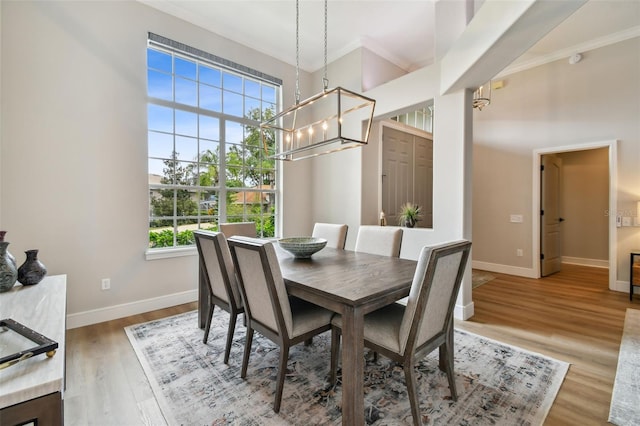 dining area featuring a high ceiling, baseboards, light wood finished floors, and ornamental molding