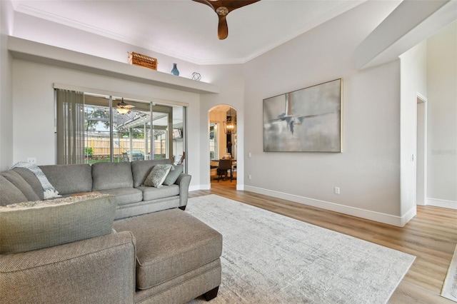 living area with crown molding, baseboards, wood finished floors, arched walkways, and a ceiling fan