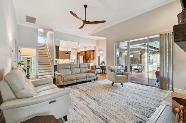 living room featuring light wood finished floors, visible vents, baseboards, ceiling fan, and stairway