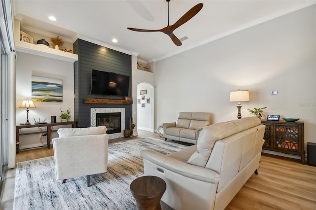 living room with a fireplace, recessed lighting, arched walkways, light wood-style floors, and crown molding